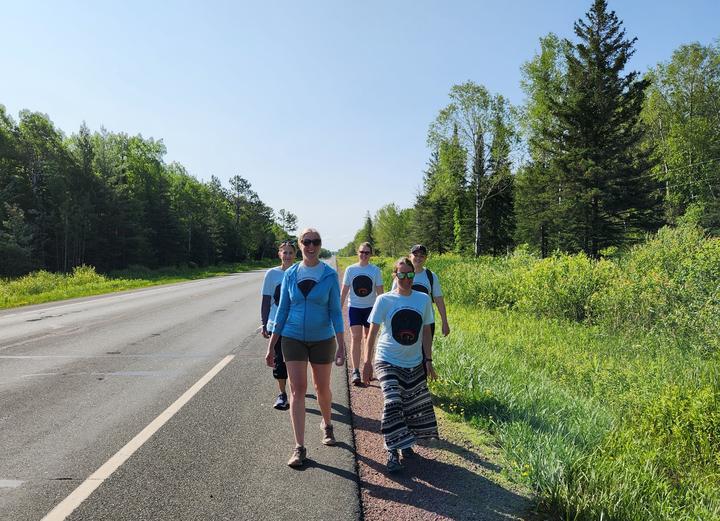 Group of people wearing matching blue shirts walk along a road