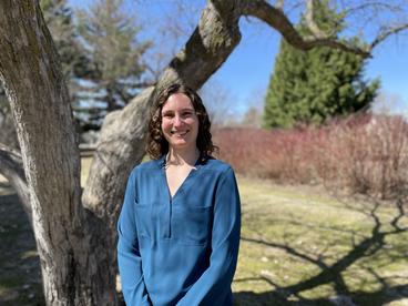 Ally Scott, wearing a blue shirt and standing in front of a tree. 