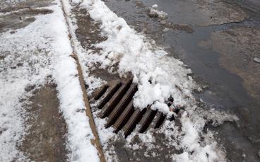 A street drain partially covered in snow